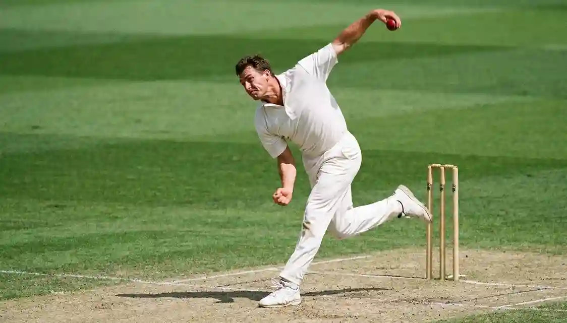 Cricket bowler in bowling action on green pitch with stumps visible