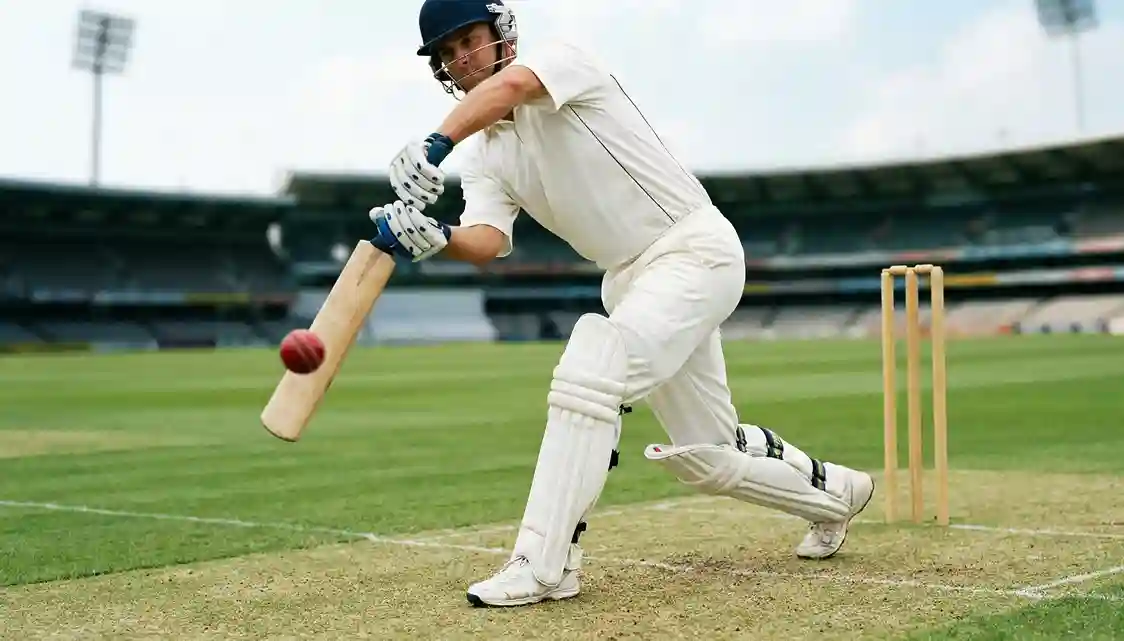 Cricket batsman in white uniform playing a powerful shot on grass pitch