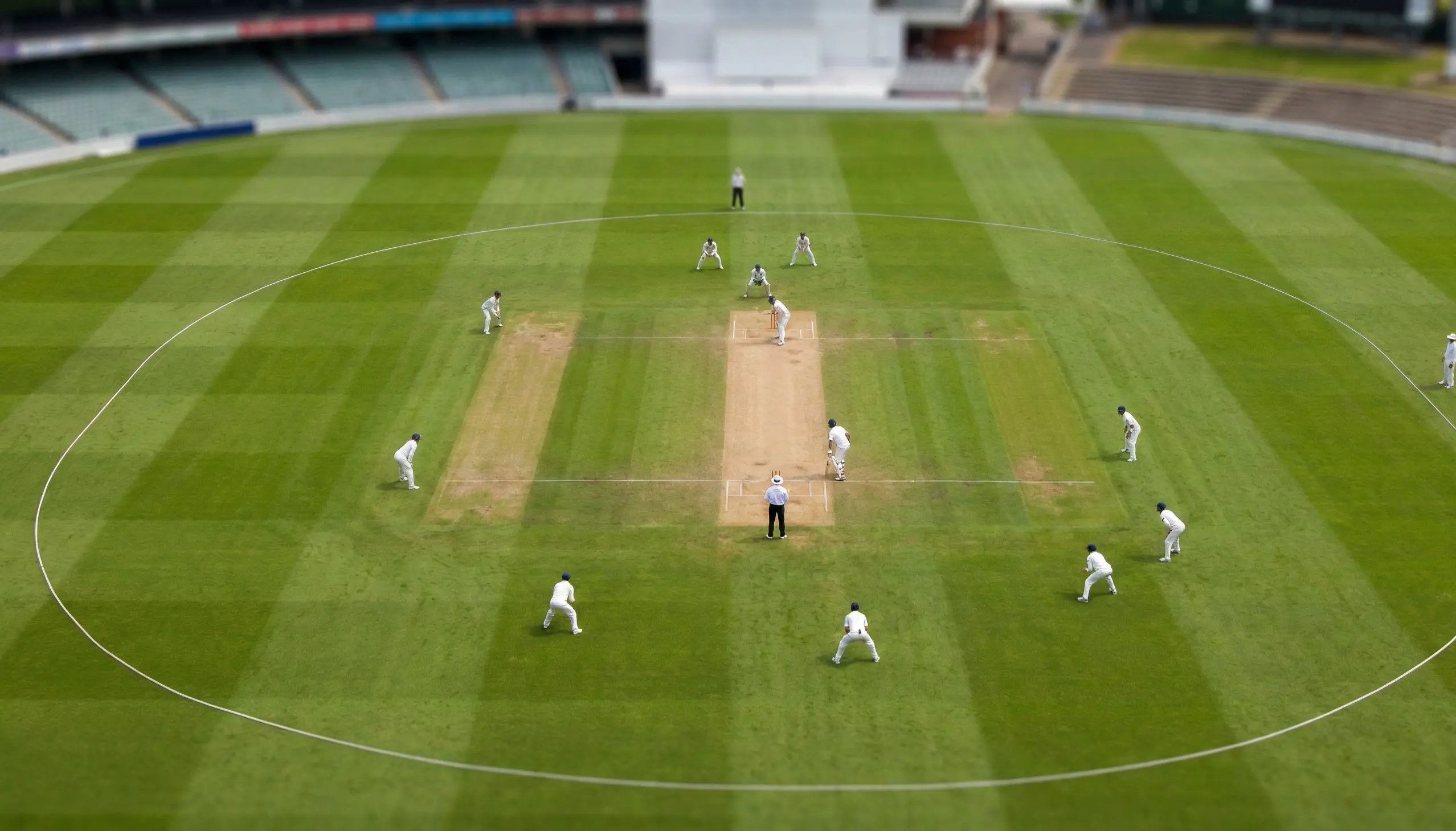 Wide view of ongoing cricket match on green oval ground with players in position